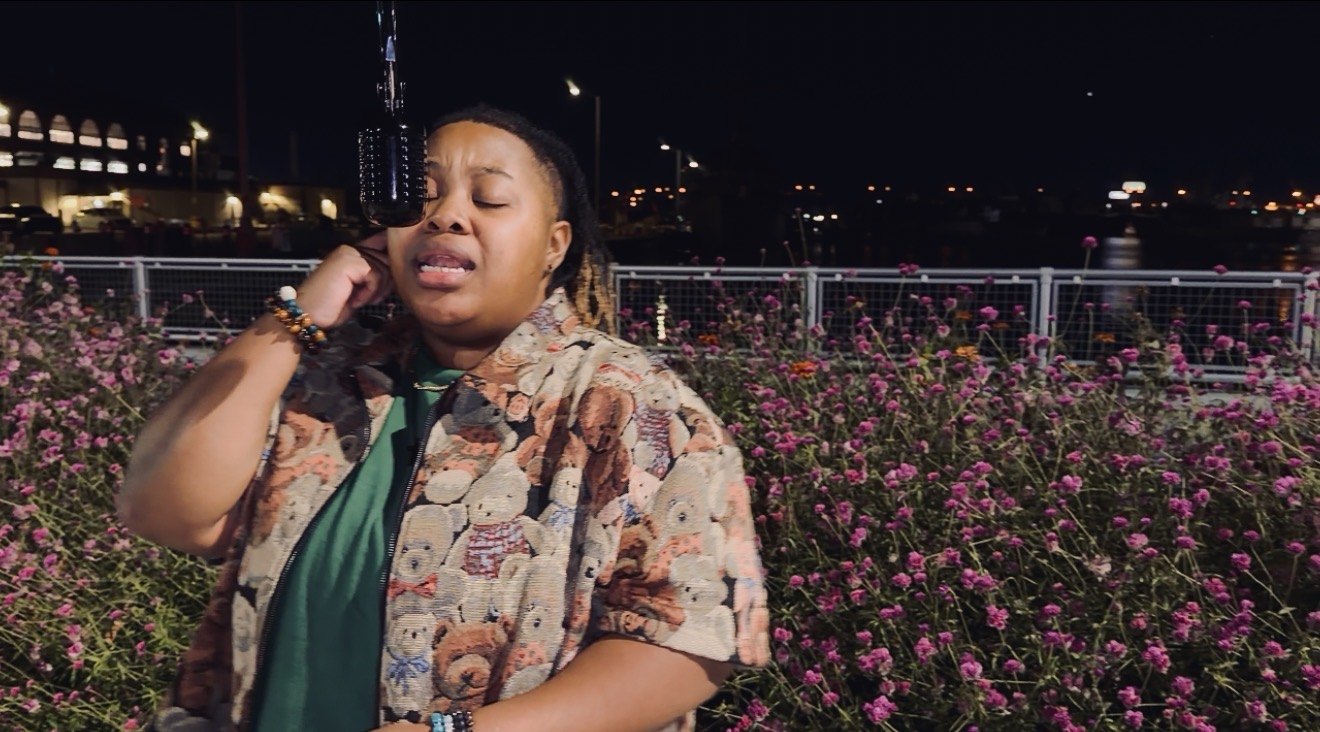 CreNaetive singing with eyes closed beside the microphone, pink flowers behind her